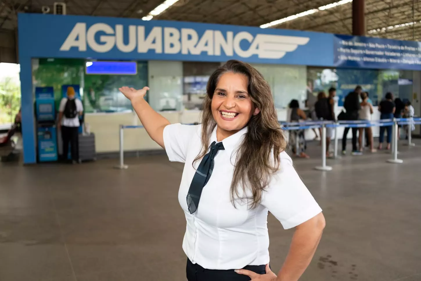 Imagem de uma mulher de 30 e poucos anos sorrindo mostrando ao fundo uma agencia da Águia Branca